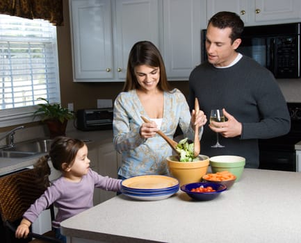 Caucasian woman making salad on kitchen counter with daughter and husband.