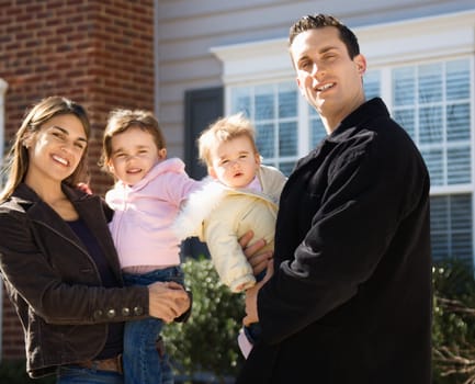 Caucasian mother and father with children standing in front of house.