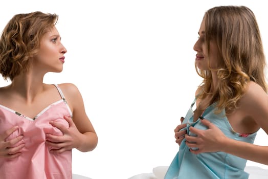 Two women stand facing each other, playfully exchanging clothing while smiling, in a bright, modern studio setting.