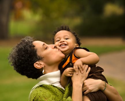 Head and shoulder portrait of woman holding and kissing boy as he smiles.