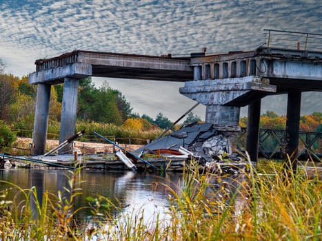 Destroyed automobile reinforced concrete bridge across the river. Destroyed road crossing over water. Road infrastructure repair. The consequences of hostilities in Ukraine.