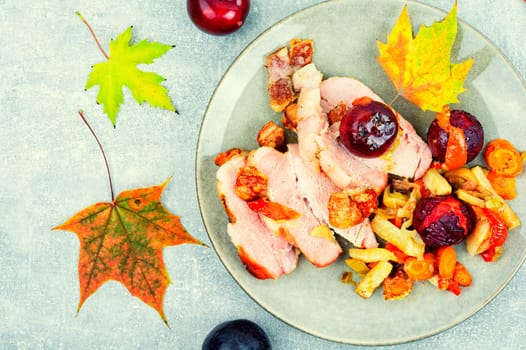 Piece of pork shoulder baked in the oven with vegetables and plums.