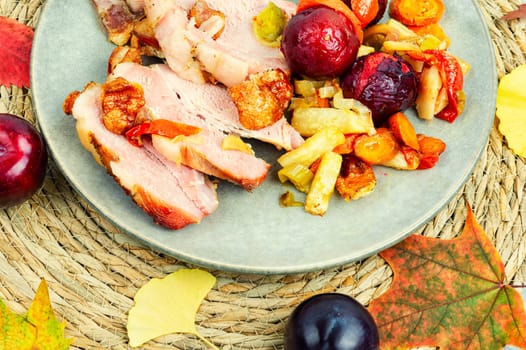 Piece of pork shoulder baked in the oven with vegetables and plums.