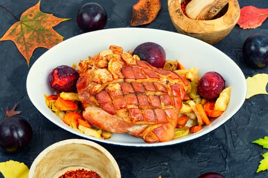 Piece of pork shoulder baked in the oven with vegetables and plums.