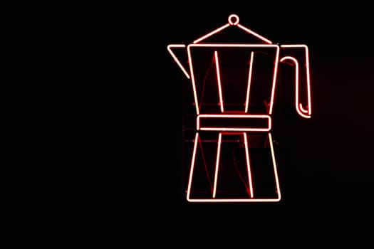 Red neon sign from lamps in the form of a Moka pot coffee maker on the wall of a black coffee shop.