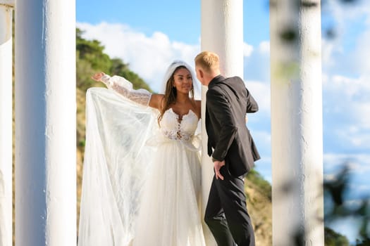 Newlyweds in a beautiful gazebo with columns against the backdrop of mountains and sky