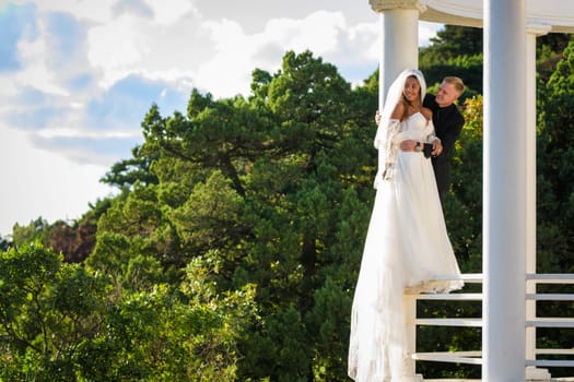 Happy newlyweds stand on the metal fence of the gazebo and look into the distance