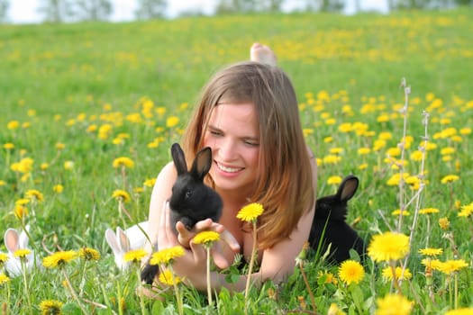 Beautiful young girl lays in grass and plays with cute small rabbits