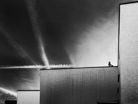 Architectural view with row house roof edges in front of a cloudless sky angled with contrails in black and white appearance.