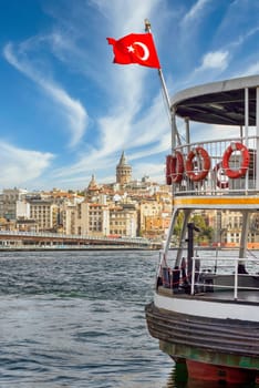 Turkish flag on a ferry boat, docked at Eminonu ferry terminal, Bosporus Strait, with skyline of Istanbul city, Turkey, in the background including Galata Tower, and Galata Bridge
