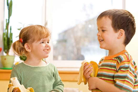 Happy little girl and boy eating bananas