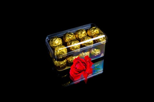 Gift box of chocolates and a red rose flower on a black background. Box of candies. Red rose flower. Golden color. Flowers and gifts. Valentine's Day. The beauty. Festive gift for a woman.