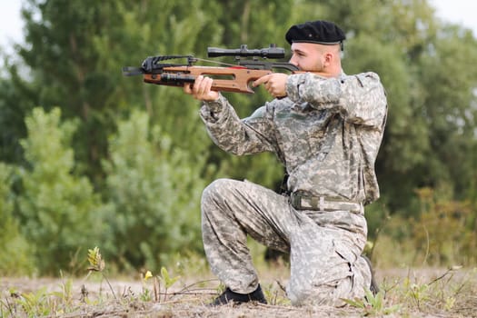 The army soldier or hunter in military uniform is aiming and shooting with crossbow weapon outdoors in nature.