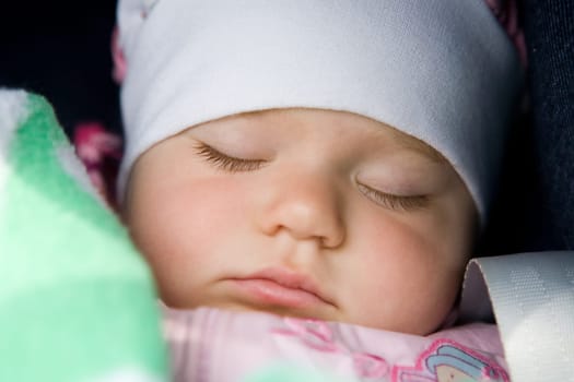 A portrait of the sleeping beautiful little girl in a white scarf close up.