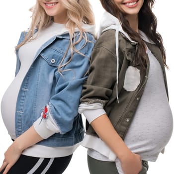 Two pregnant women showcase trendy jackets while posing together, celebrating motherhood with smiles and joy in a relaxed setting.