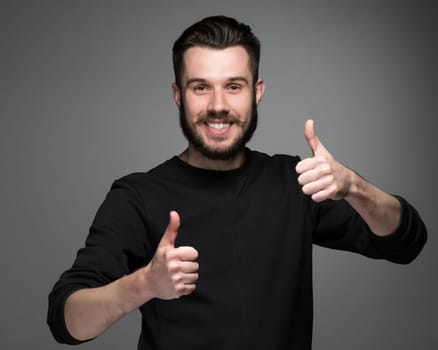 Closeup portrait of handsome young smiling man, giving a raised finger on gray background. Positive human emotions