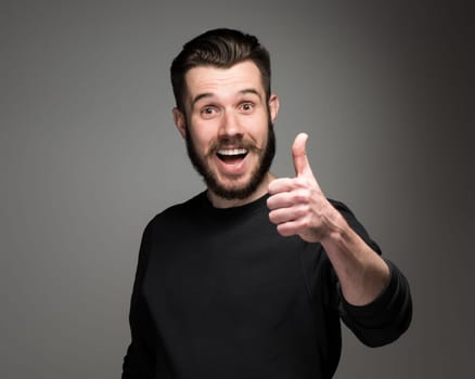 Closeup portrait of handsome young smiling man, giving a raised finger on gray background. Positive human emotions