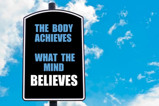 THE BODY ACHIEVES WHAT THE MIND BELIEVES  motivational quote written on road sign isolated over clear blue sky background with available copy space. Concept  image