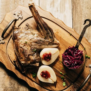 High Angle View of Roasted Venison Haunch on Wooden Tray with Prepared Pears on Rustic Table