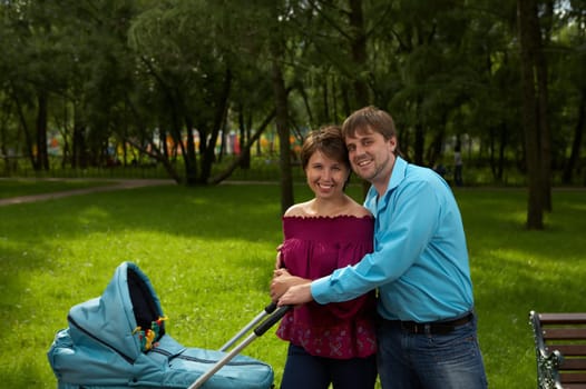 Happy parents with newborn in a pram walk in park