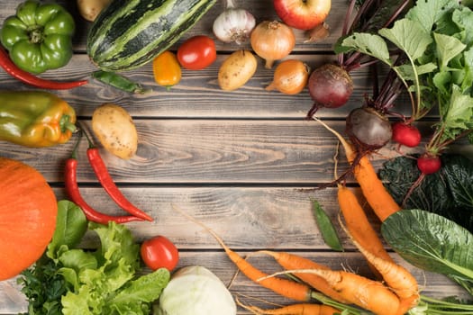 Colorful mix of fresh farm vegetables and fruits, top view. Sorting organic ripe harvest on wooden table. Nitrate free food or healthy diet concept. Objects circular arrangement. Cooking ingredients.