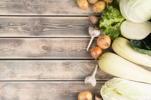 Vertical row of fresh farm vegetables on wooden table, top view. Seasonal foodstuffs sorting. Nitrate free food or healthy diet concept. Objects layout. Planking. Cooking ingredients. Place for text.