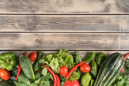 Horizontal row of fresh farm vegetables on wooden table, top view. Foodstuffs arrangement. Nitrate free food or healthy diet concept. Objects layout. Planking. Cooking ingredients. Place for text.