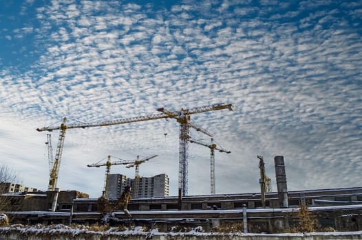 High-rise cranes are building a new house. Construction high-rise crane. New houses. Industrial landscape. Multi-storey building. Blue sky with white cumulus clouds. City life.