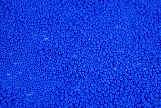 The texture of the surface of scattered blue beads for needlework. Beads for women's needlework. Blue round granules. Textured effect. Background image. Template for text.