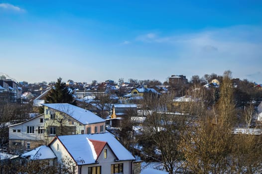 Snow-covered roofs of rural houses against the blue sky. Rural houses. Winter season. Blue sky. Cumulus clouds. White sneh. Cloudy horizon. Winter landscape. Background image.