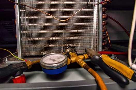 Filling an industrial refrigeration unit with freon. Refrigerator repair. Hand tool. Cooling pipeline. Cooling radiator. Pressure gauge and hoses. Screwdrivers and pliers. Refrigerator service.