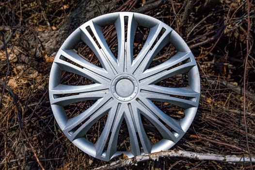 Silver plastic car wheel rim cap. Part of a car wheel. Detail of the vehicle. Tire service. Branches of a tree. Background image. Place for your text. Industrial waste. Garbage dump. Ecology.