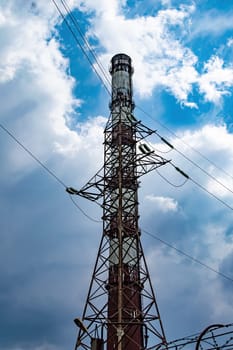 High voltage tower with wires and industrial chimney. High-voltage transmission line of electrical energy. Chimney of the enterprise. Industrial landscape. Cloudy sky horizon. Background.