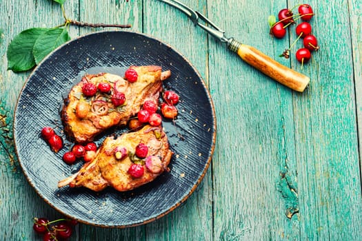 Two cooked steaks in a cherry marinade. Fried meat with berry sauce on old wooden background. Space for text