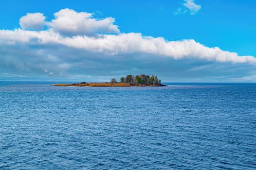 Uninhabited island in the sea against a blue sky with clouds. Island with trees. Sea horizon. Blue sky with clouds. Ocean water wave. Natural base. background image. Endless expanses of water.
