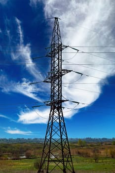 High-voltage power transmission tower with wires. High voltage line. Energy industry. Energy transfer. Blue sky. White clouds. Agricultural field. Cloudy horizon. Business. Electrician work.