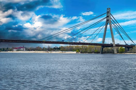 Bridge over the Dnieper River in Kiev against a cloudy sky. Car crossing over water. Bridge over the river. Water flow. Blue sky. Thunderclouds. Background. Industrial architecture.