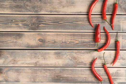 Vertical line of red hot peppers on faded wooden table, top view. Spicy chillies arranged in order. Organic food or healthy diet concept. Location of objects. Planking. Place for text.