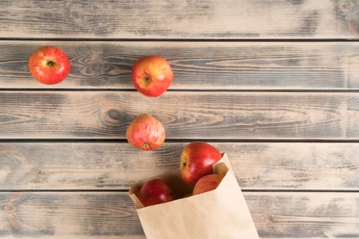 Bunch of fragrant sweet red apples on faded wooden table, top view. Fresh garden fruits take out of eco paper bag. Organic food or healthy diet concept. Planking. Nitrate free nutrition.