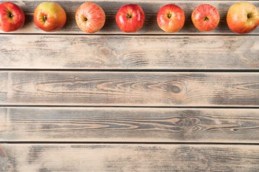 Horizontal line of fragrant sweet red apples on faded wooden table, top view. Fresh appetizing garden fruits arranged in order. Organic food or healthy diet concept. Planking. Place for text.
