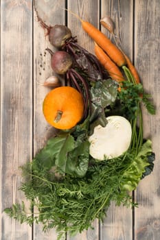 Bunch of greens and different seasonal vegetables with long green haulm on wooden table, top view. Farm fresh harvest, vitamins. Nitrate free food or healthy diet concept. Objects layout. Planking.