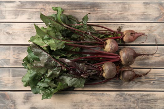 Bunch of fresh ripe beets with long green haulm on faded wooden table, top view. Prepare unpeeled raw beetroots for cooking. Organic food or healthy diet concept. Objects layout. Planking.