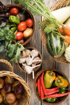 Wicker baskets with different fresh garden vegetables on wooden table, top view. Bowls full of organic ripe harvest. Food or healthy diet concept. Nitrate free nutrition. Cooking ingredients.