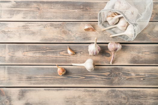 Bunch of unpeeled garlic on faded wooden table, top view. Eco fabric poach full of aromatic spice. Food or healthy diet concept. Separated location of garlic cloves. Planking. Culinary and cooking.