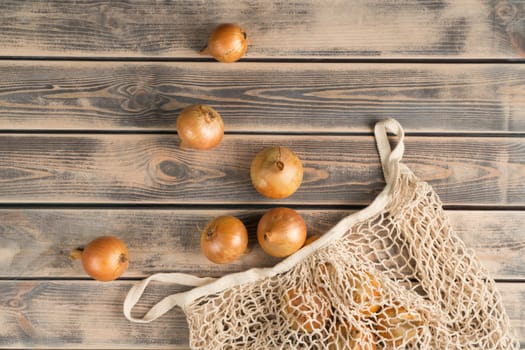 Bunch of unpeeled white onions on faded wooden table, top view. Farm vegetables take out from eco fabric mesh bag. Food or healthy diet concept. Separated location. Planking. Culinary and cooking.