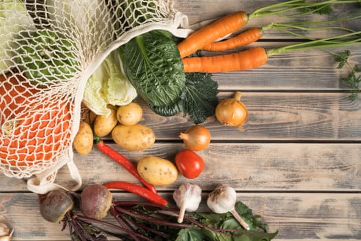 Variety of fresh farm vegetables on wooden table, top view. Unpacking foodstuffs from mesh fabric bag. Nitrate free food or healthy diet concept. Objects layout. Planking. Cooking ingredients.