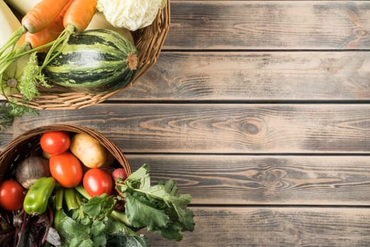 Two wicker baskets with different fresh farm vegetables on gray wooden table, top view. Bowls full of ripe harvest. Food or healthy diet concept. Planking. Place for text. Nitrate free nutrition.