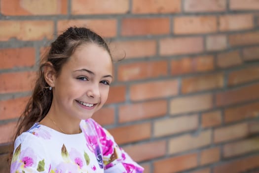 Portrait of pretty little girl  smiling at the camera. Brick wall is in the background. Horizontally.