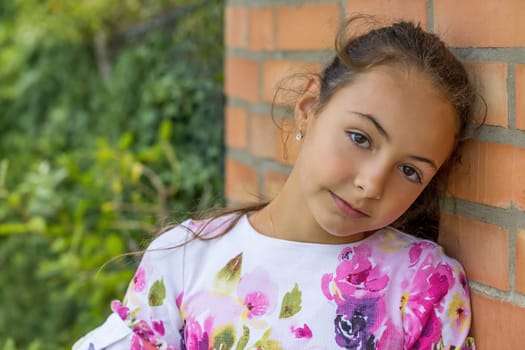 Cute little girl poses with her head resting on a brick wall. Horizontally.