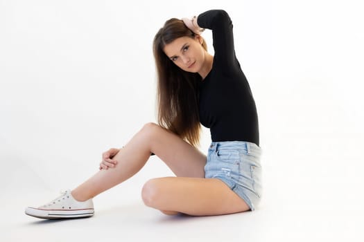 Young long haired and long legged woman is posing  sitting on floor and looking at camera.